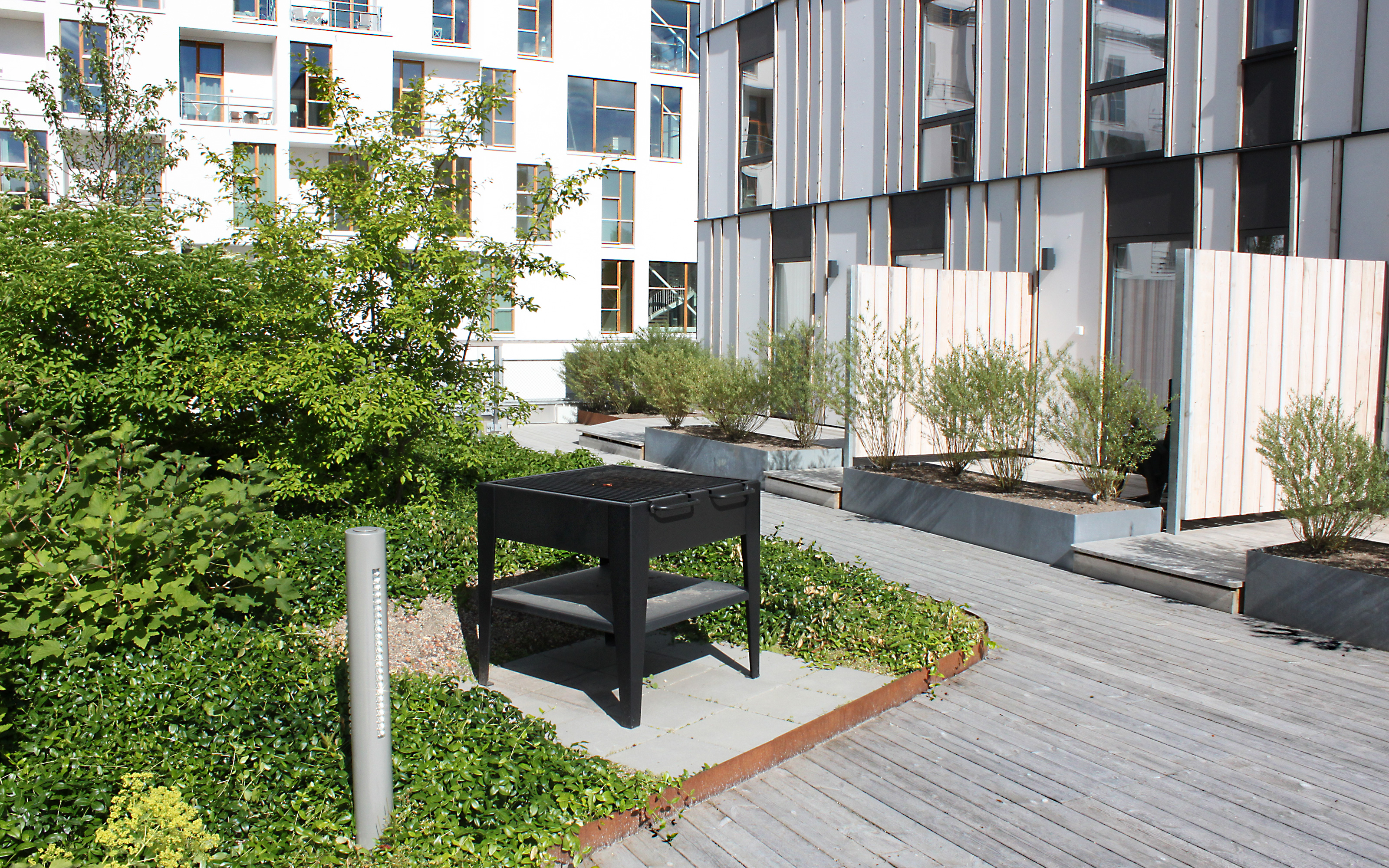Moveable public furniture can be arranged freely near one of the fixed barbecue places. Green courtyard with barbecue place surrounded by residential buildings.